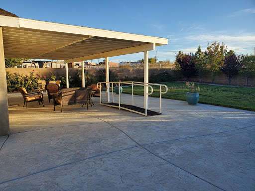 A serene outdoor patio area featuring comfortable seating and an accessible ramp leading to a grassy space, illuminated by the warm glow of sunset.
