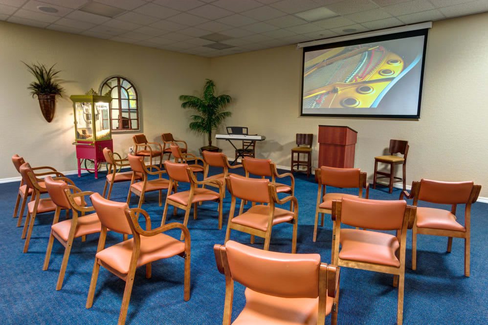 An empty conference room set up for a presentation, featuring rows of chairs, a podium, and a large projection screen.