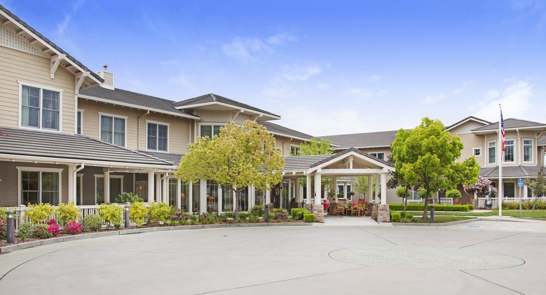 A two-story residential building with a landscaped driveway and trees.