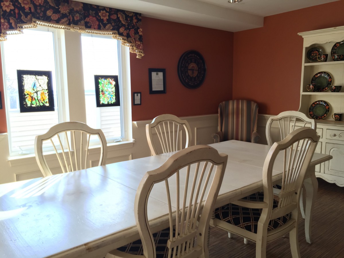 A sunlit dining room with a large table and chairs, featuring warm-colored walls and wall decor.