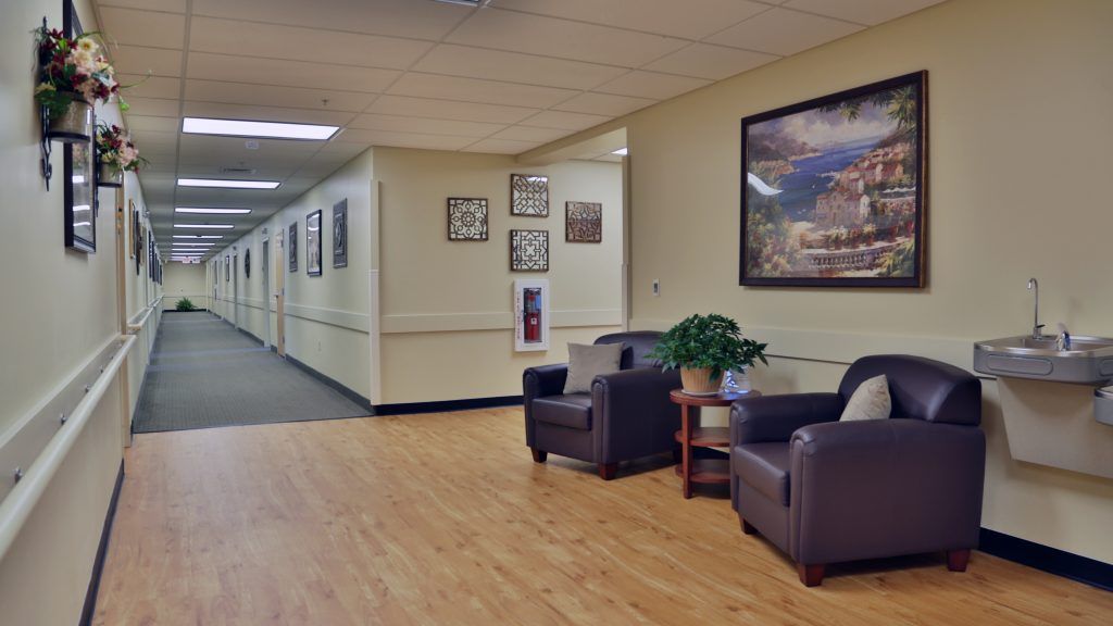 A quiet hallway with a seating area featuring two chairs, a small table, and a painting on the wall.