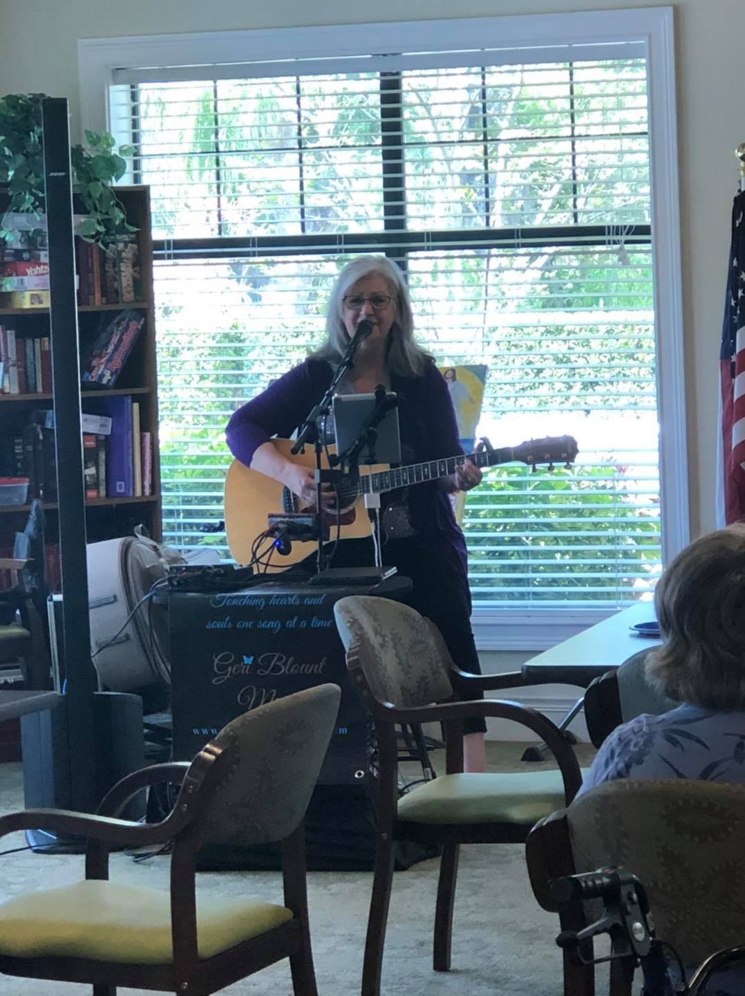 A performer plays guitar and sings for an audience in an intimate indoor setting.