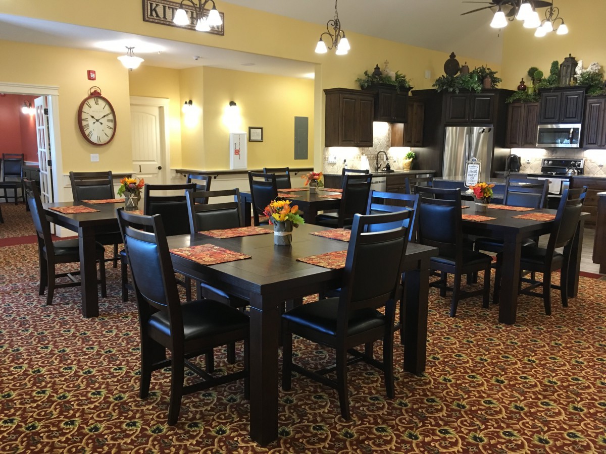 A cozy dining area with multiple tables and chairs, featuring a kitchen in the background.