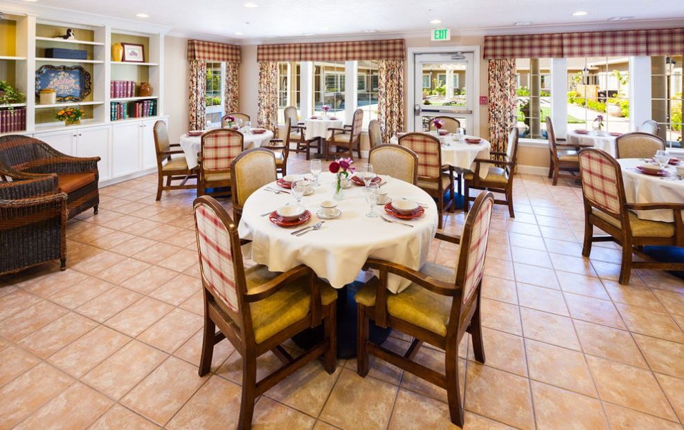 A neatly arranged dining room with round tables and upholstered chairs.