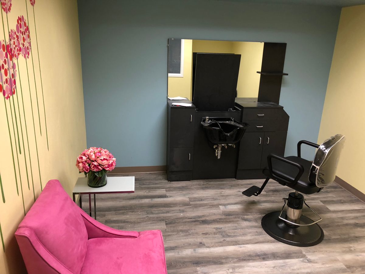A modern hair salon interior featuring a styling chair, mirror, and pink sofa with decorative flowers.