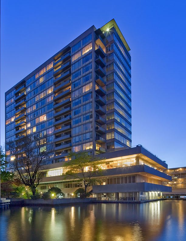 A modern skyscraper illuminated at night, reflecting in the surrounding water.