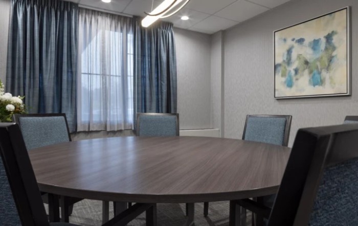 A modern conference room with a round table and chairs, complemented by curtains and wall artwork.