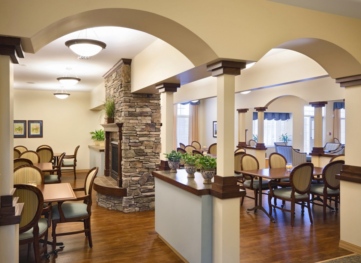 A cozy dining area with arched doorways and a stone fireplace, featuring wooden flooring and elegant furniture.