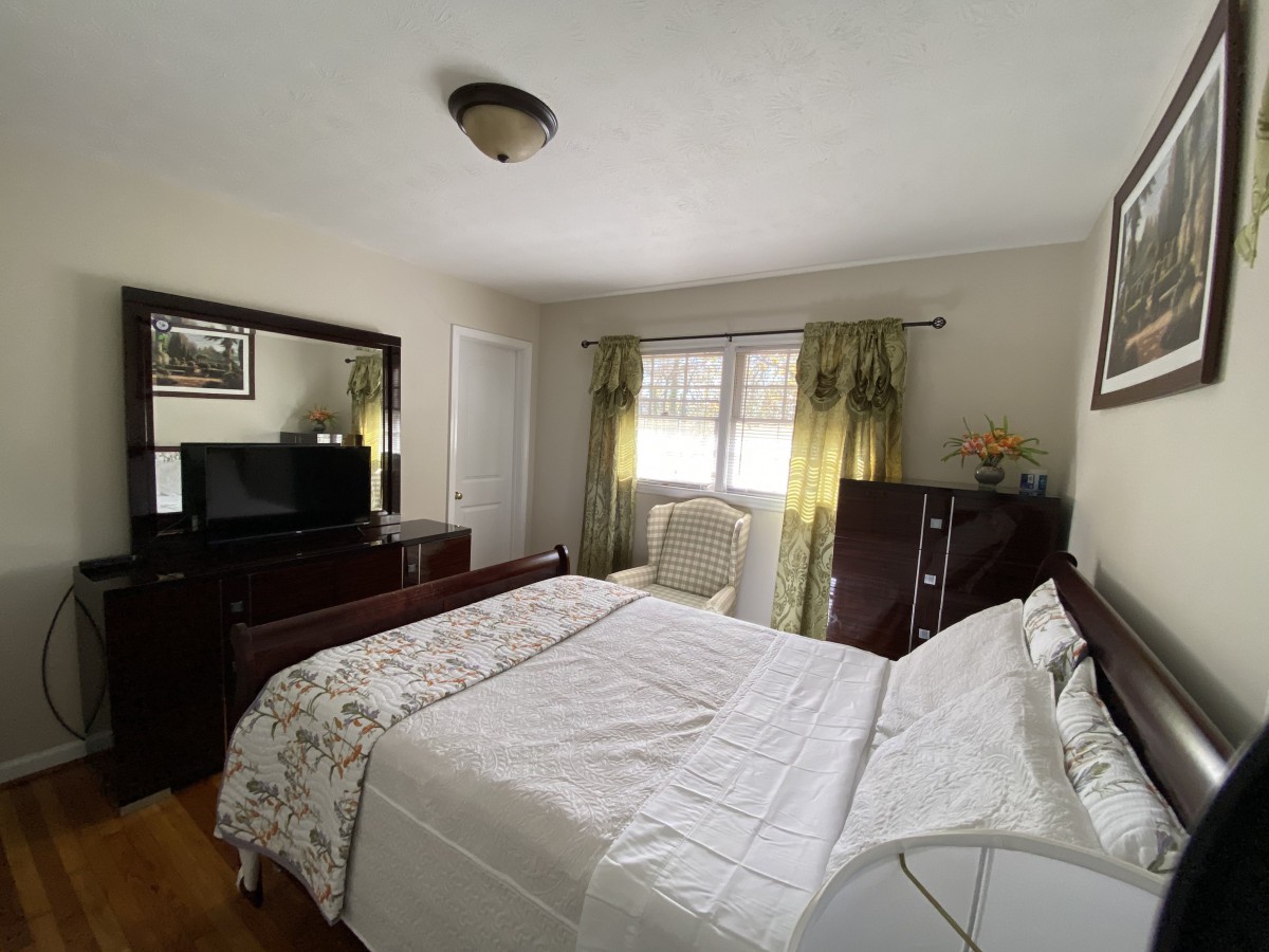 A cozy bedroom with a large bed, dresser, and window with curtains.