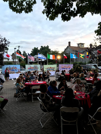 An outdoor community gathering featuring various international flags, as guests enjoy dinner in a festive atmosphere.
