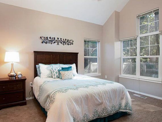 A cozy bedroom with a neatly made bed and large windows letting in natural light.