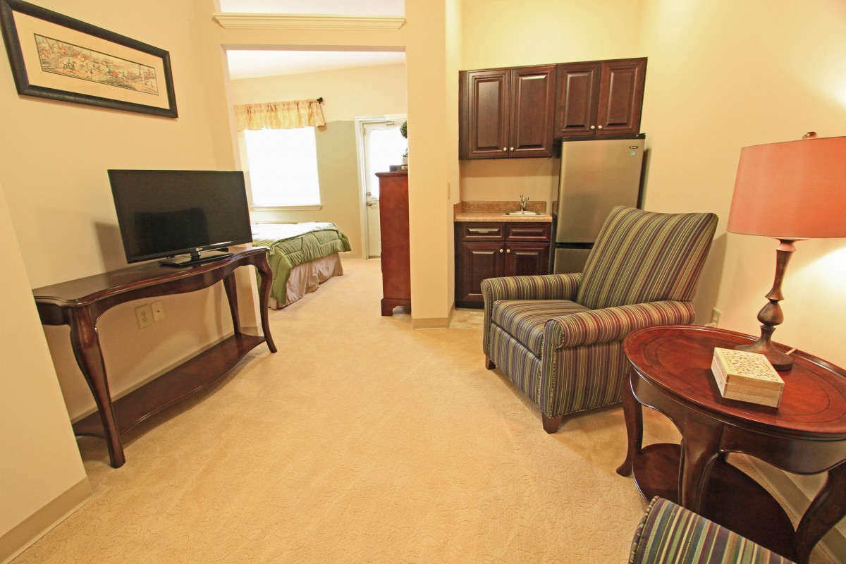 A cozy living room area with an armchair, TV, and a kitchenette.