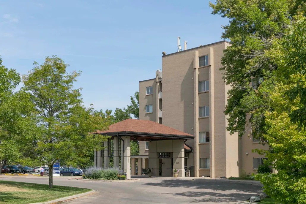 A hotel building with an entrance surrounded by trees and a driveway.