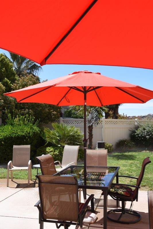 A backyard patio with red umbrellas providing shade over a table and chairs.