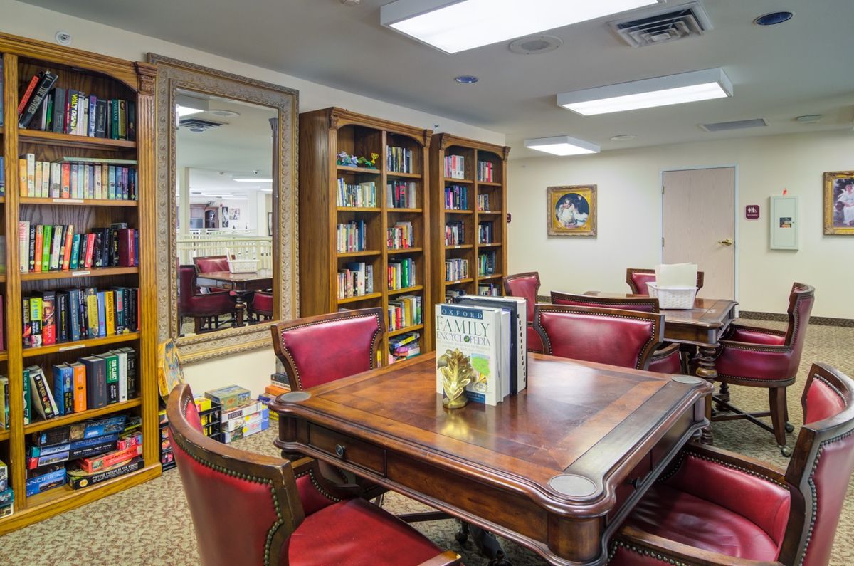 A cozy library reading room with wooden furniture, red chairs, and bookshelves filled with books.