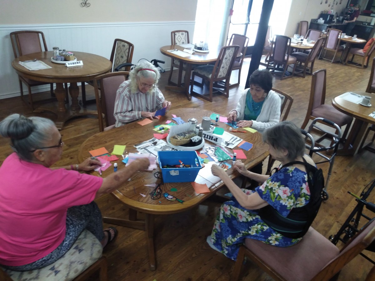 A group of elderly women engaging in craft activities at a communal table.