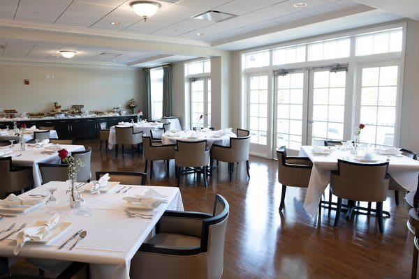 An elegant restaurant dining room with neatly arranged tables and chairs, featuring large windows that allow natural light to fill the space.