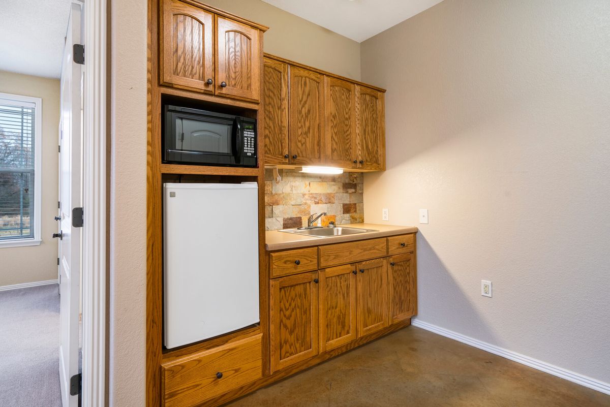 A small kitchenette with wooden cabinets, a microwave, and a mini fridge.