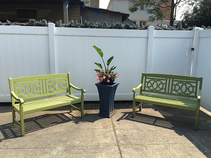 Two green benches flank a potted plant in an outdoor garden setting.