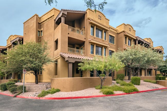 A modern residential apartment building with landscaped surroundings and a warm color palette.