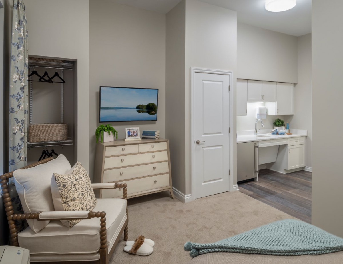 A modern bedroom with neutral colors featuring a dresser, TV, and comfortable seating.