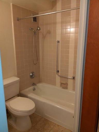 A compact bathroom featuring a bathtub with a shower, toilet, and tiled walls.