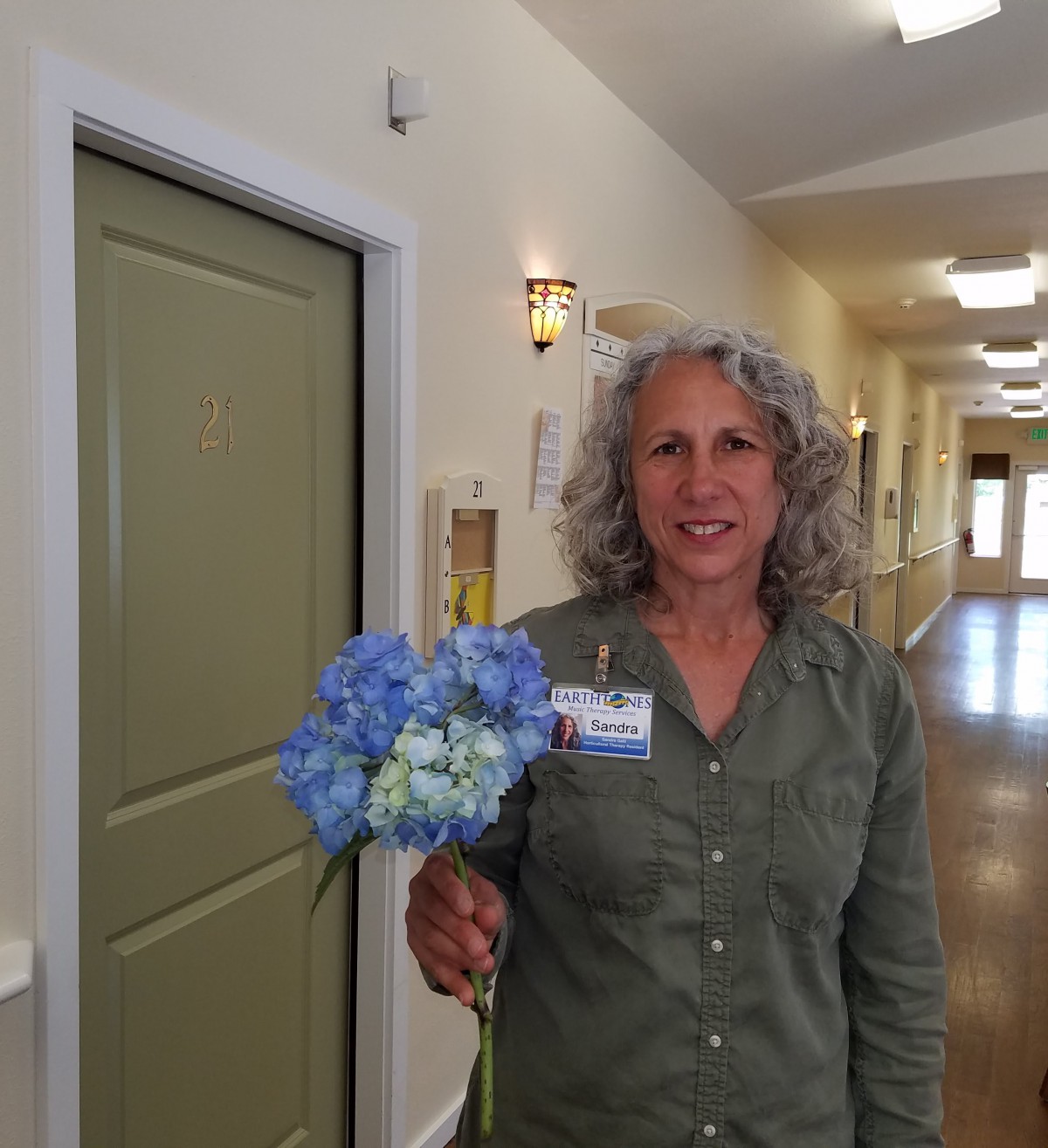A woman standing in a hallway holding a bouquet of blue flowers.