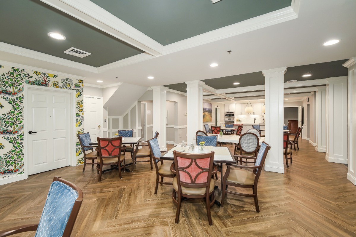 A well-lit dining area with wooden flooring, featuring multiple tables and chairs arranged for guests.