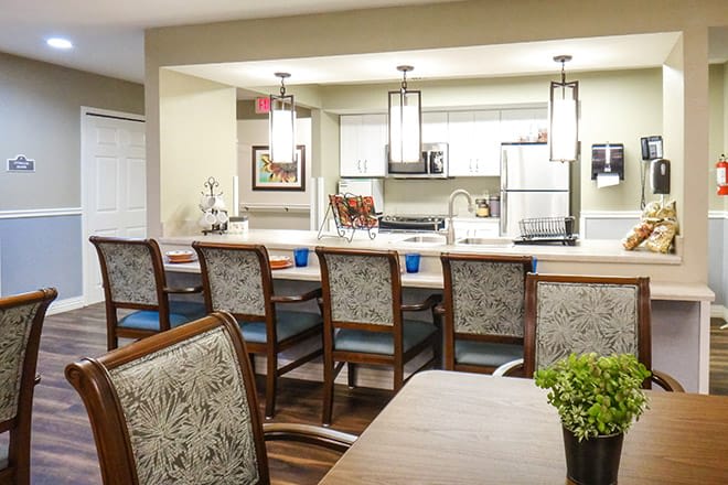 A modern kitchen and dining area featuring a large counter with several chairs, illuminated by stylish pendant lights.