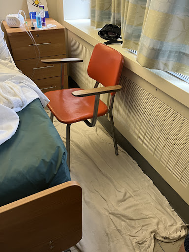 A view of a hospital patient room featuring an orange chair beside a bed.