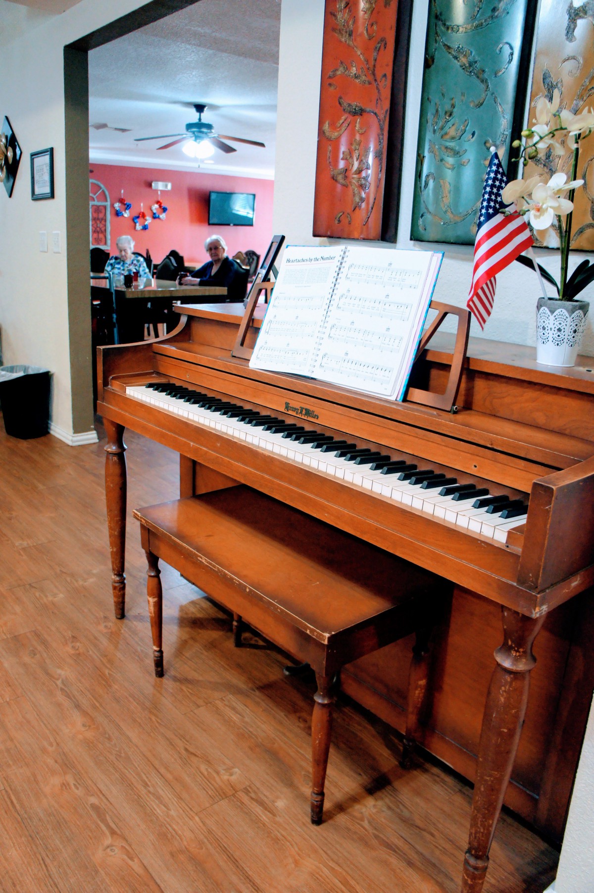A wooden piano with sheet music displayed on the stand, accompanied by a small American flag.