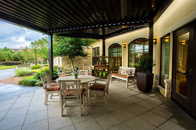A cozy outdoor patio with seating under a pergola, surrounded by greenery.