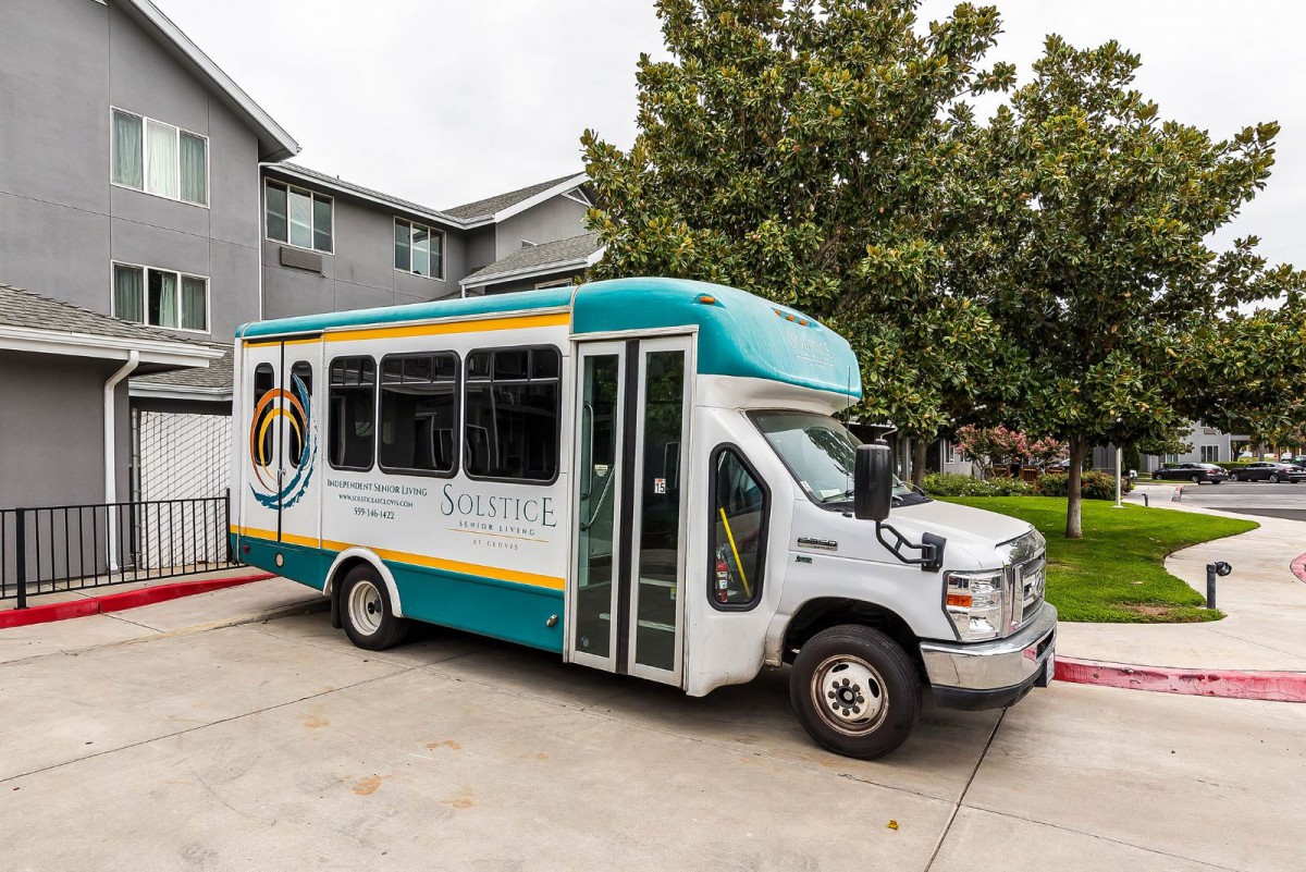 A shuttle bus parked in a residential area next to a building and trees.