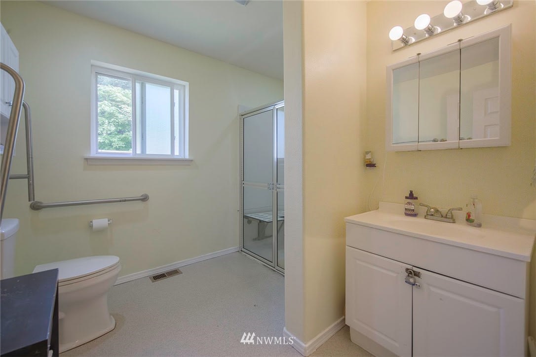 A clean, minimalist bathroom featuring a toilet, shower, and vanity with mirror.
