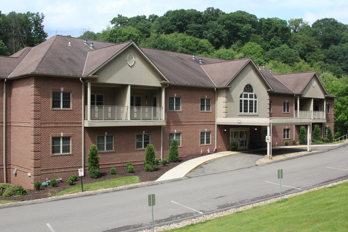 A residential building surrounded by greenery with a driveway leading to the entrance.