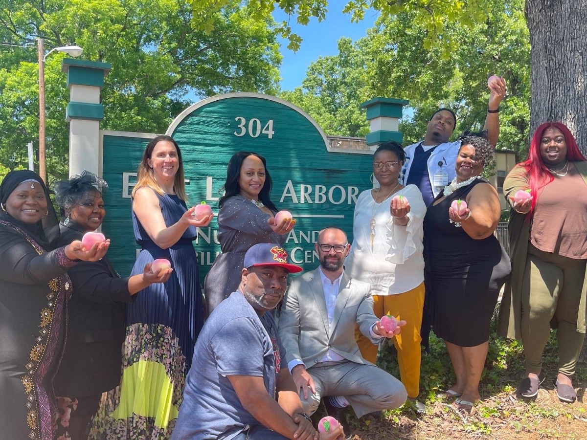 A group of people smiling and posing in front of a sign on a sunny day.