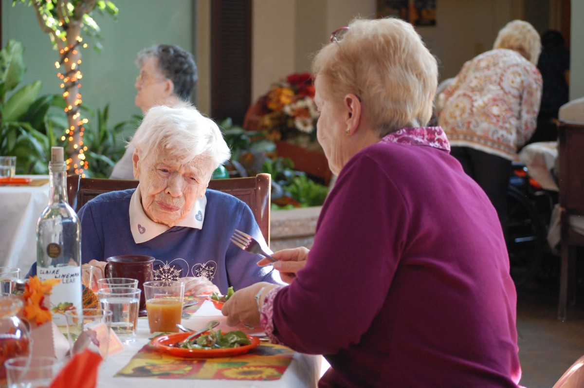 Two elderly women enjoying a meal and conversing at a table.