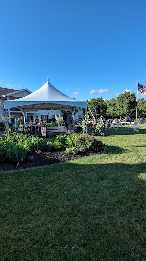 A tent set up for an outdoor event surrounded by lush greenery and a clear blue sky.