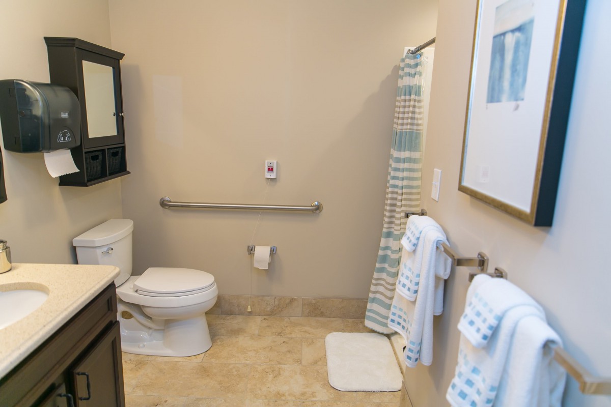 A clean and well-organized bathroom featuring a toilet, sink, towels, and a shower with a striped curtain.