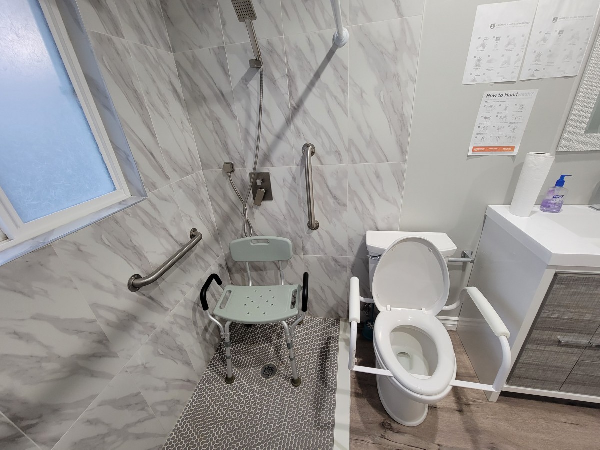 An accessible bathroom with a shower chair and toilet equipped with grab bars.