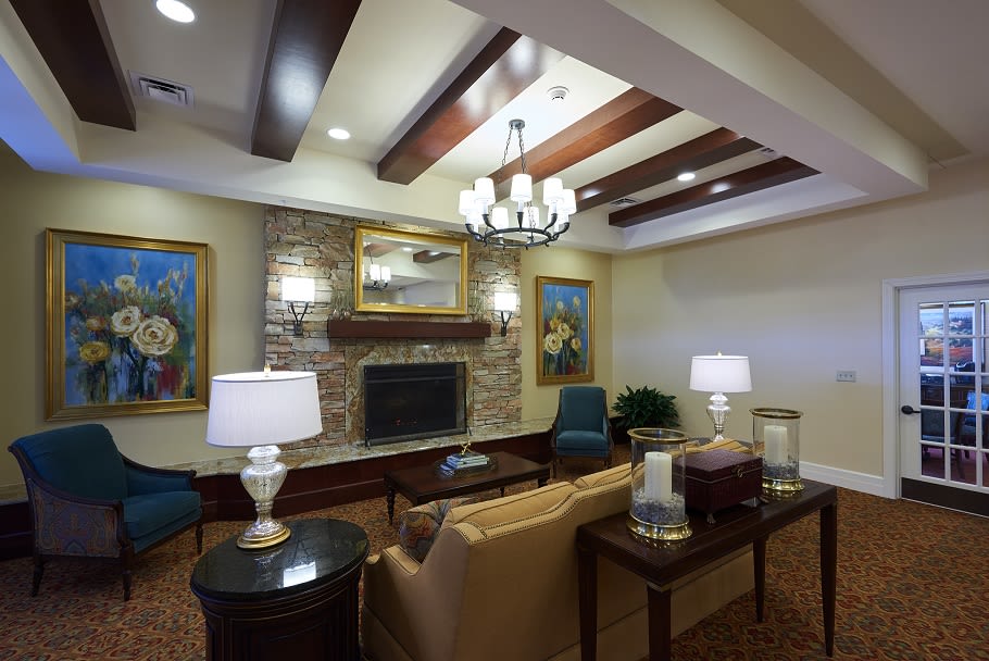 A cozy living room featuring a stone fireplace, elegant chandelier, and comfortable seating arrangements accented by classic decor elements.