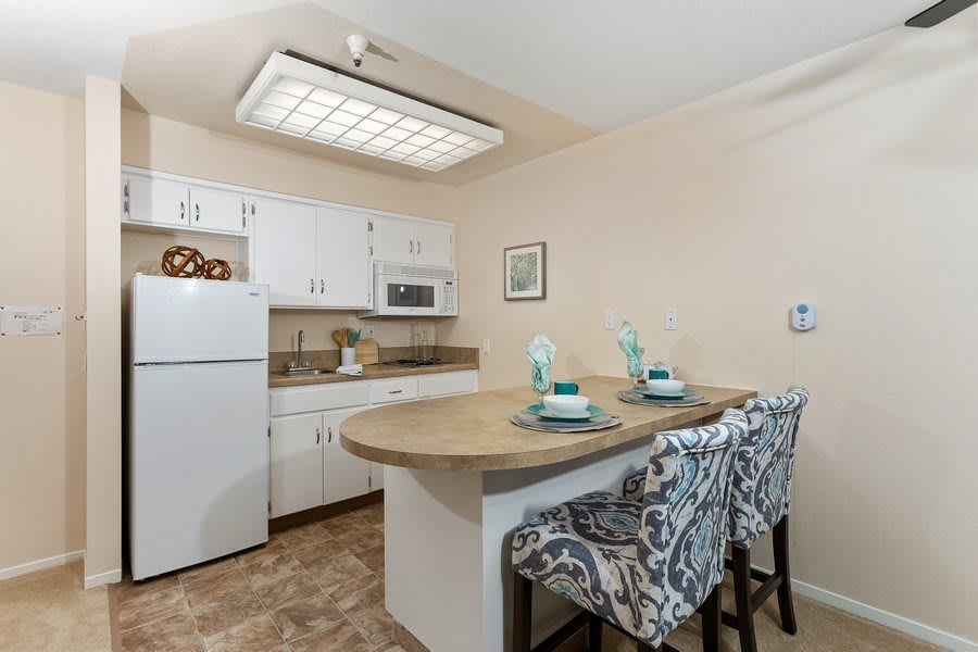 A modern kitchen with white cabinets, a central countertop, and stylish bar stools.