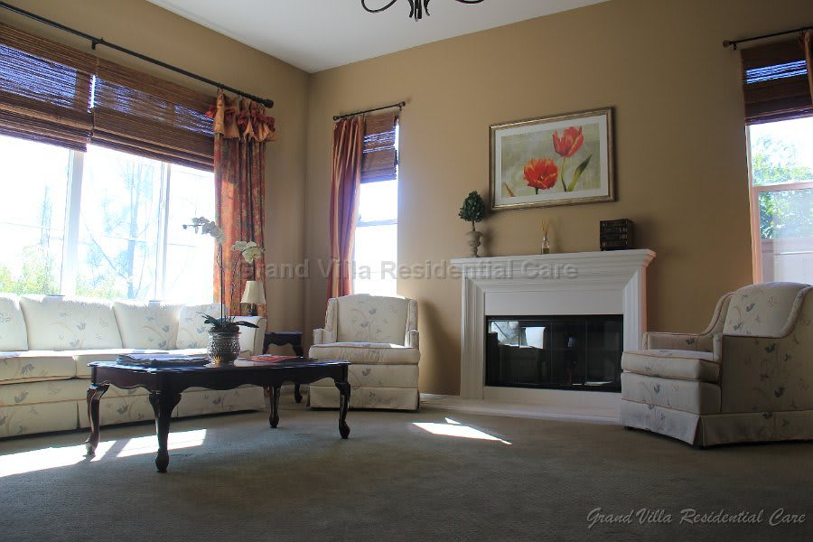A cozy living room featuring a fireplace, armchairs, and a coffee table, with natural light streaming through the windows.