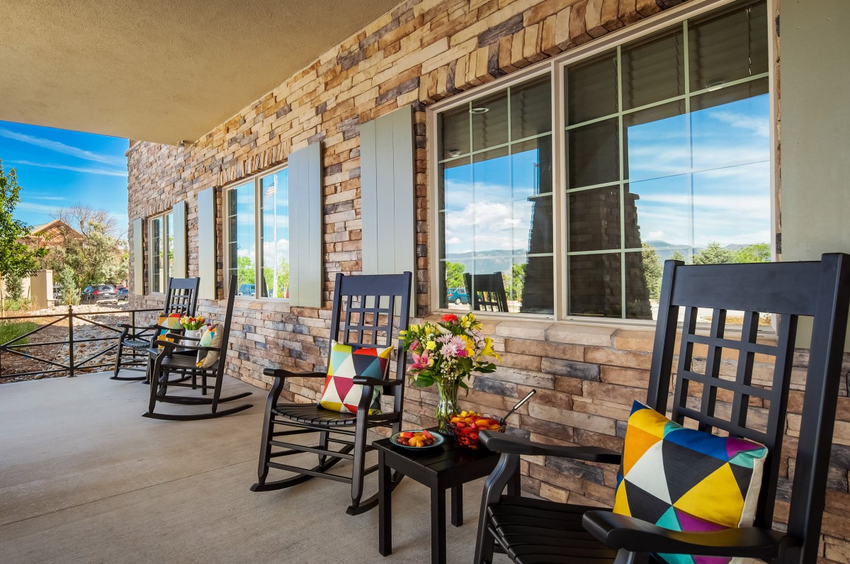 A cozy porch with rocking chairs adorned with colorful cushions, set against a brick wall and under bright windows.