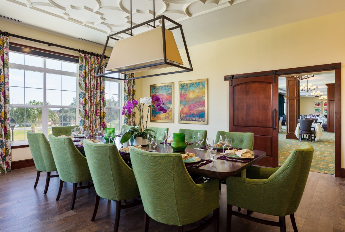 A beautifully designed dining room featuring green upholstered chairs, a modern hanging light fixture, and vibrant artwork on the wall.