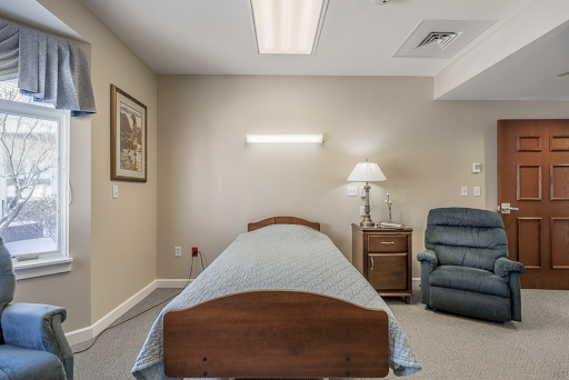 A simple and serene room featuring a single bed, a comfy chair, and soft lighting.