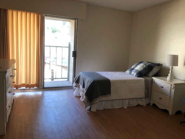 A minimalist bedroom with a double bed, adjacent to a sliding door leading to a balcony.