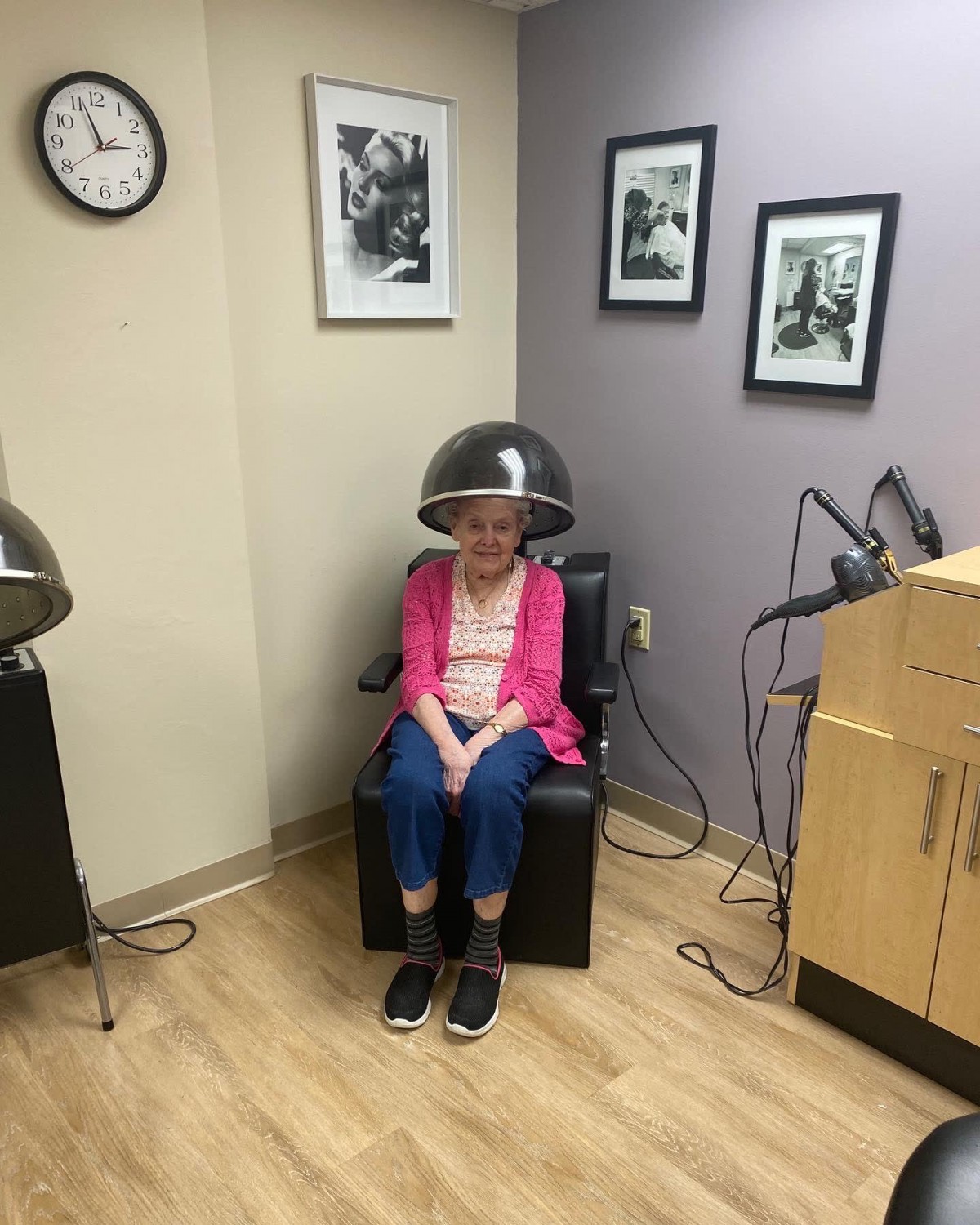 A person sitting under a vintage hair dryer in a salon.