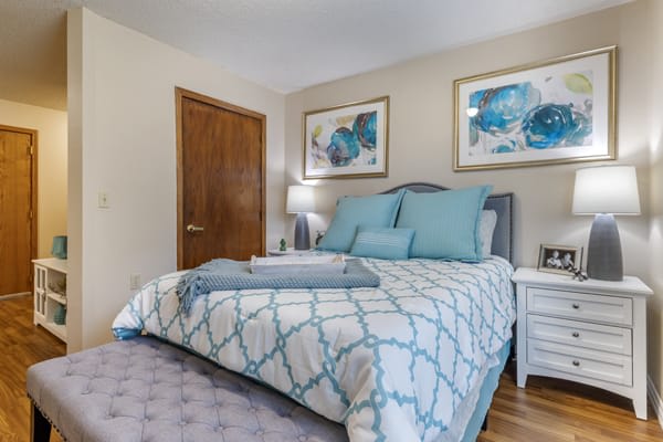 A cozy bedroom with a neatly made bed, decorated with blue and white bedding and complemented by artwork on the walls.