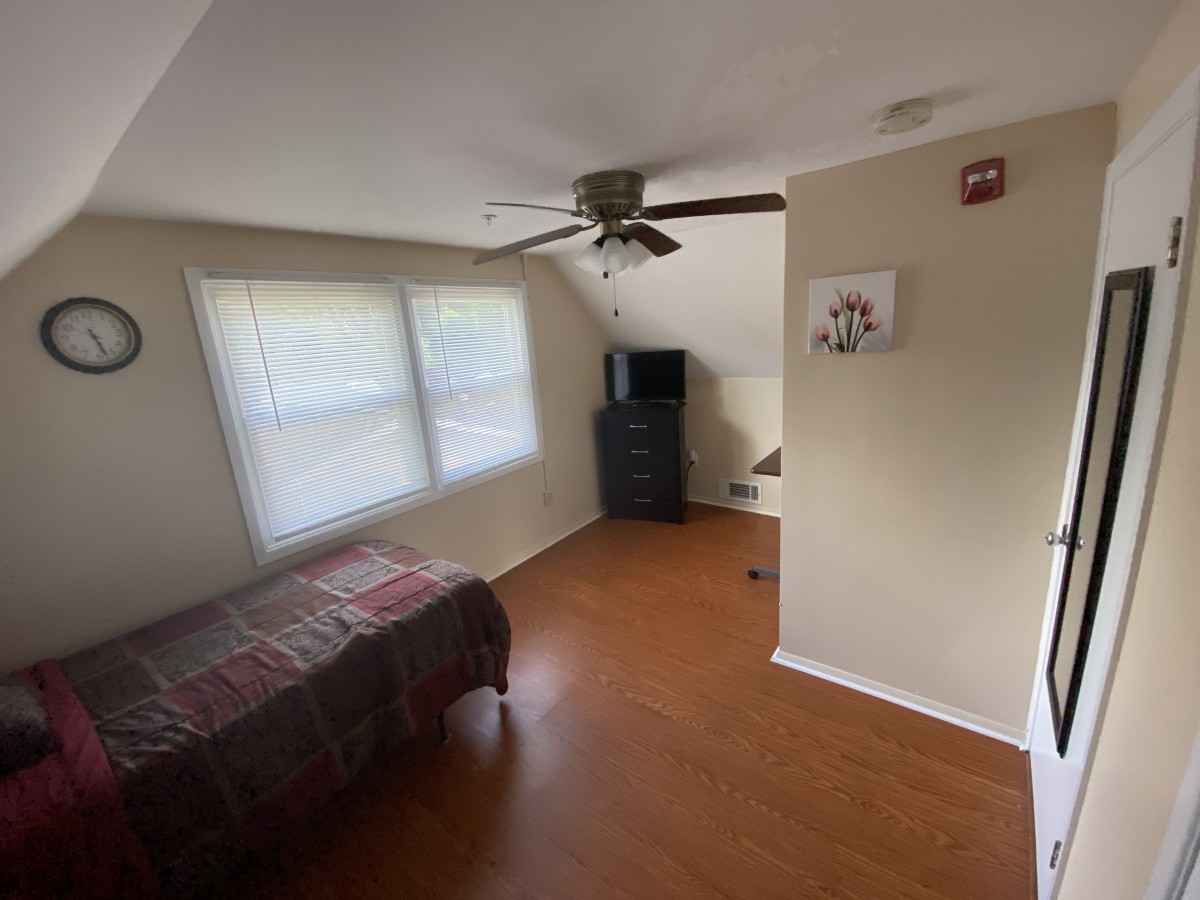 A cozy bedroom with a bed, window, dresser, and ceiling fan.